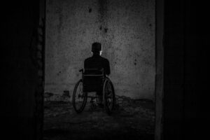 homem sentado na cadeira de rodas, virado para uma parede, sozinho em um ambiente escuro.