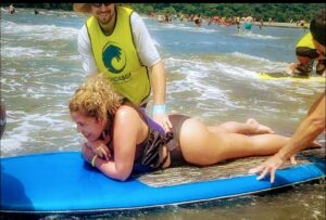 Sú Almeida deitada sob uma prancha de surf em um dia de praia acessível no litoral paulista
