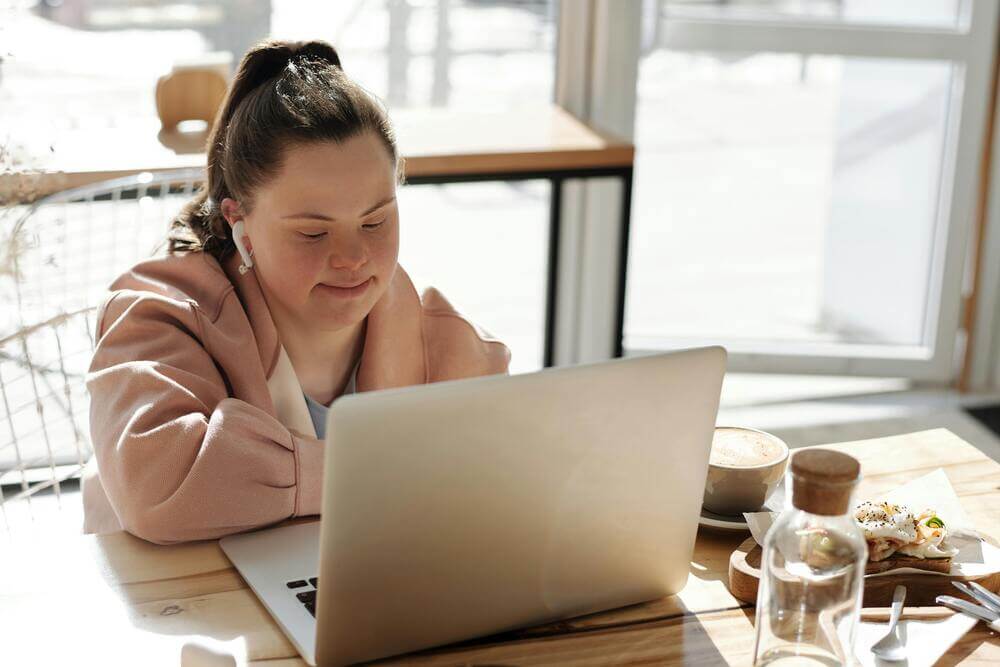 mulher com síndrome de down sentada em uma mesa acessando um notebook consulta a lei do deficiente intelectual.